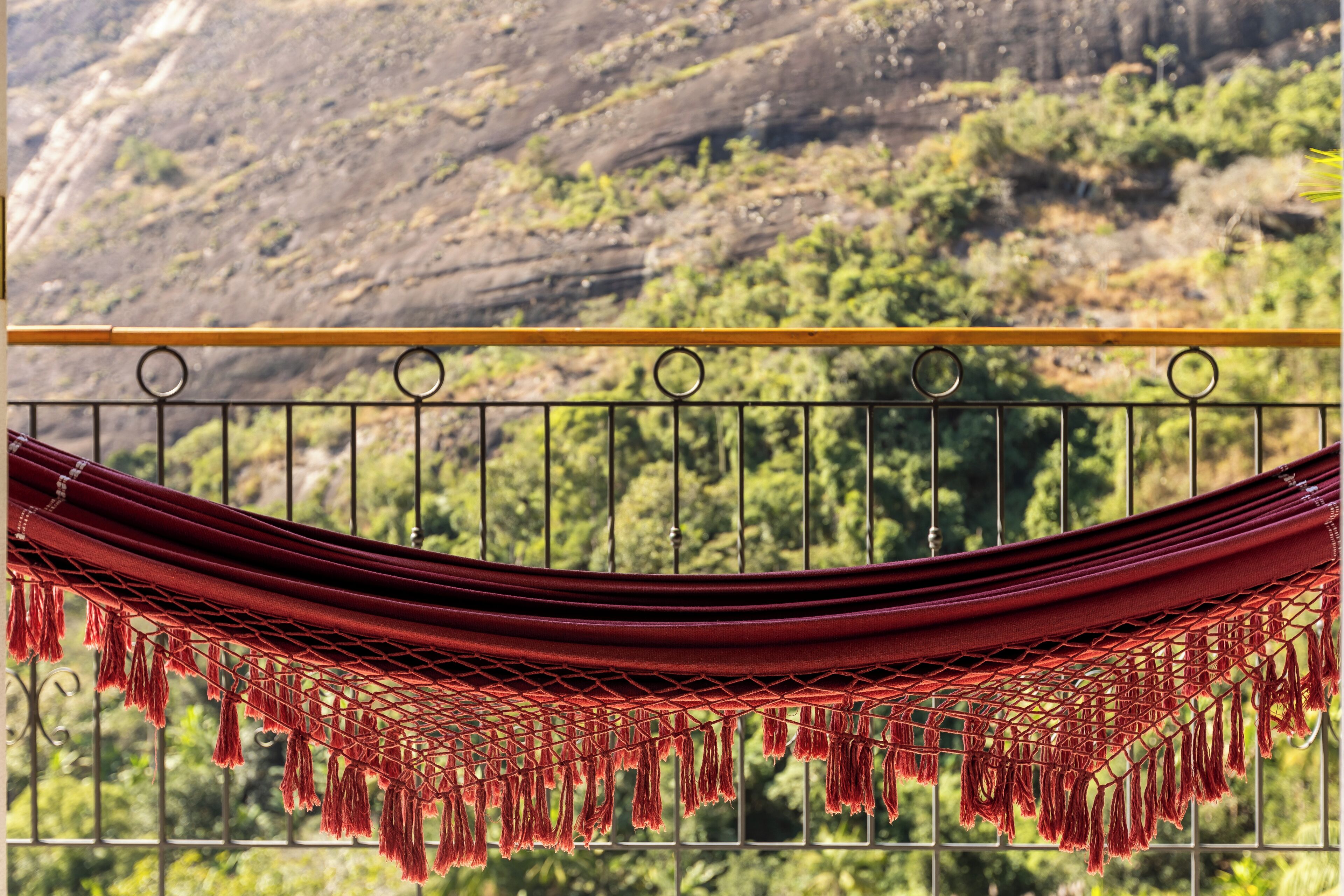 A hammock suspended over a metal railing with a mountainous landscape in the background.