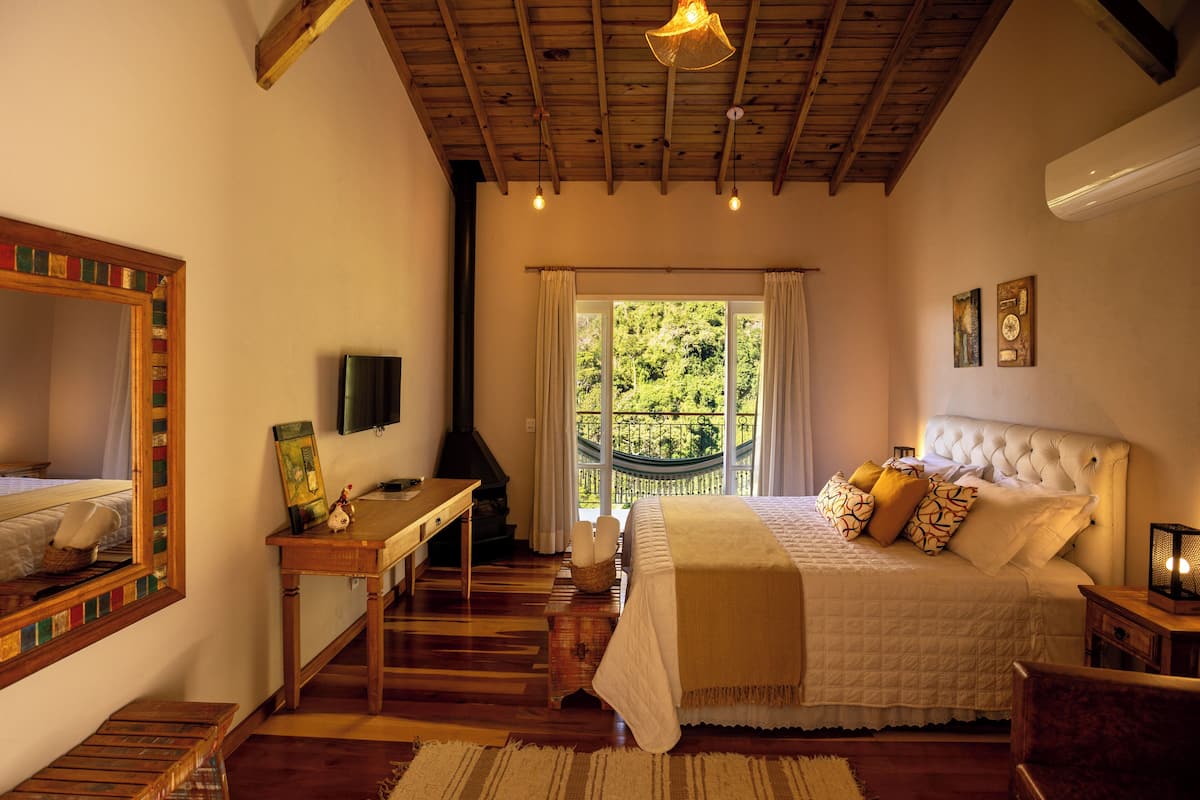 Een slaapkamer met een houten plafond, een bed met wit beddengoed, een houten bureau en een raam met gordijnen.