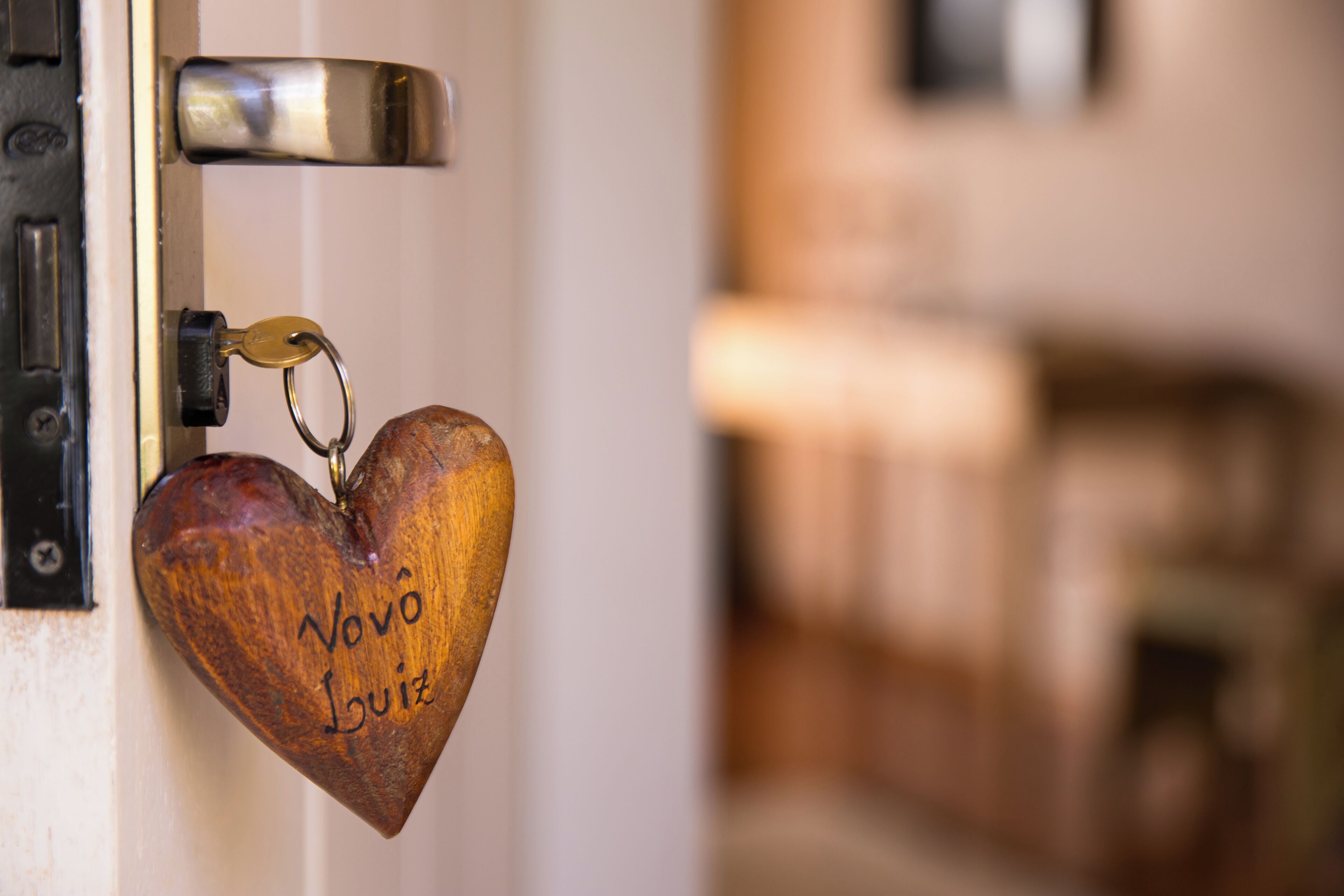 A wooden heart-shaped keychain with "Vovo Luiz" engraved on it, hanging on a door lock.