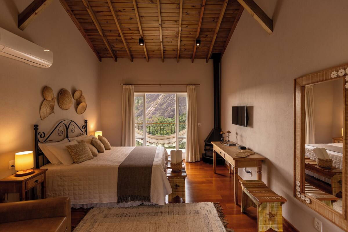 Een slaapkamer met een bed, bedlampen, een bureau, een spiegel en uitzicht op het groen.