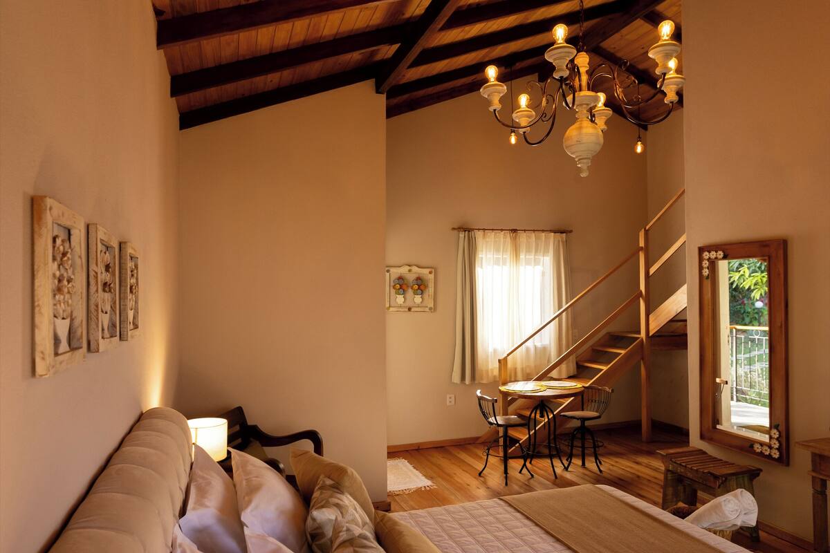 Een slaapkamer met een groot bed, een houten plafond en een trap naar een hoger gelegen verdieping.