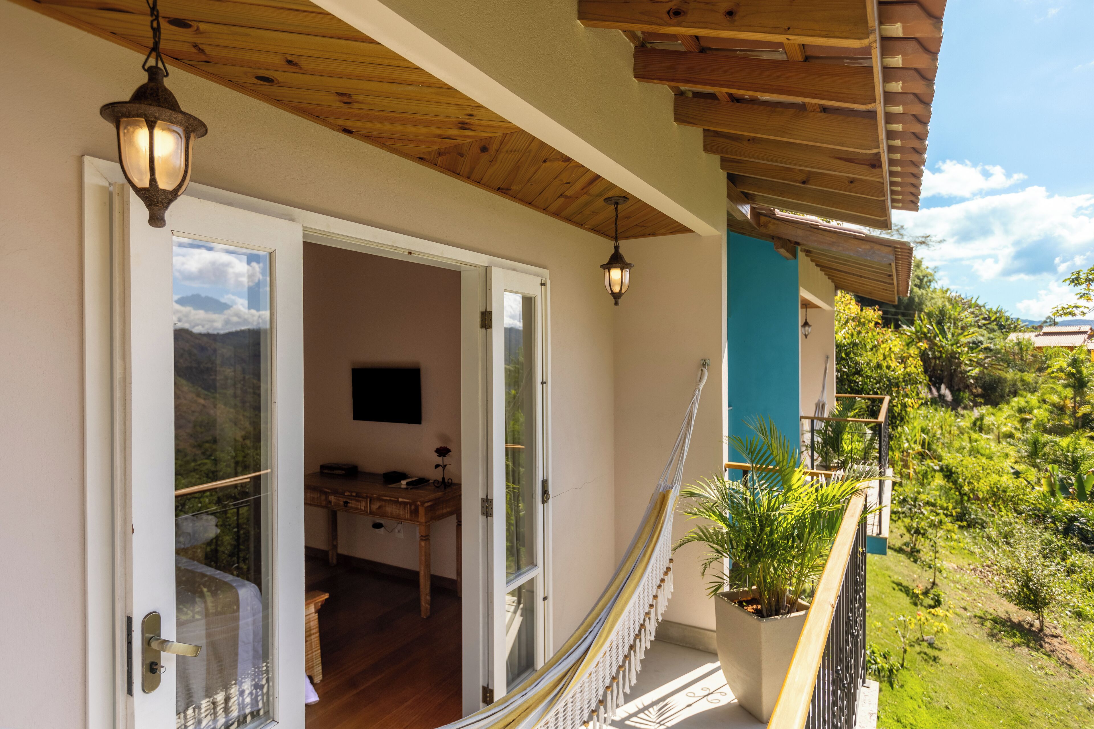 Uma varanda com guarda-corpo de madeira, um vaso com planta e vista para o verde.