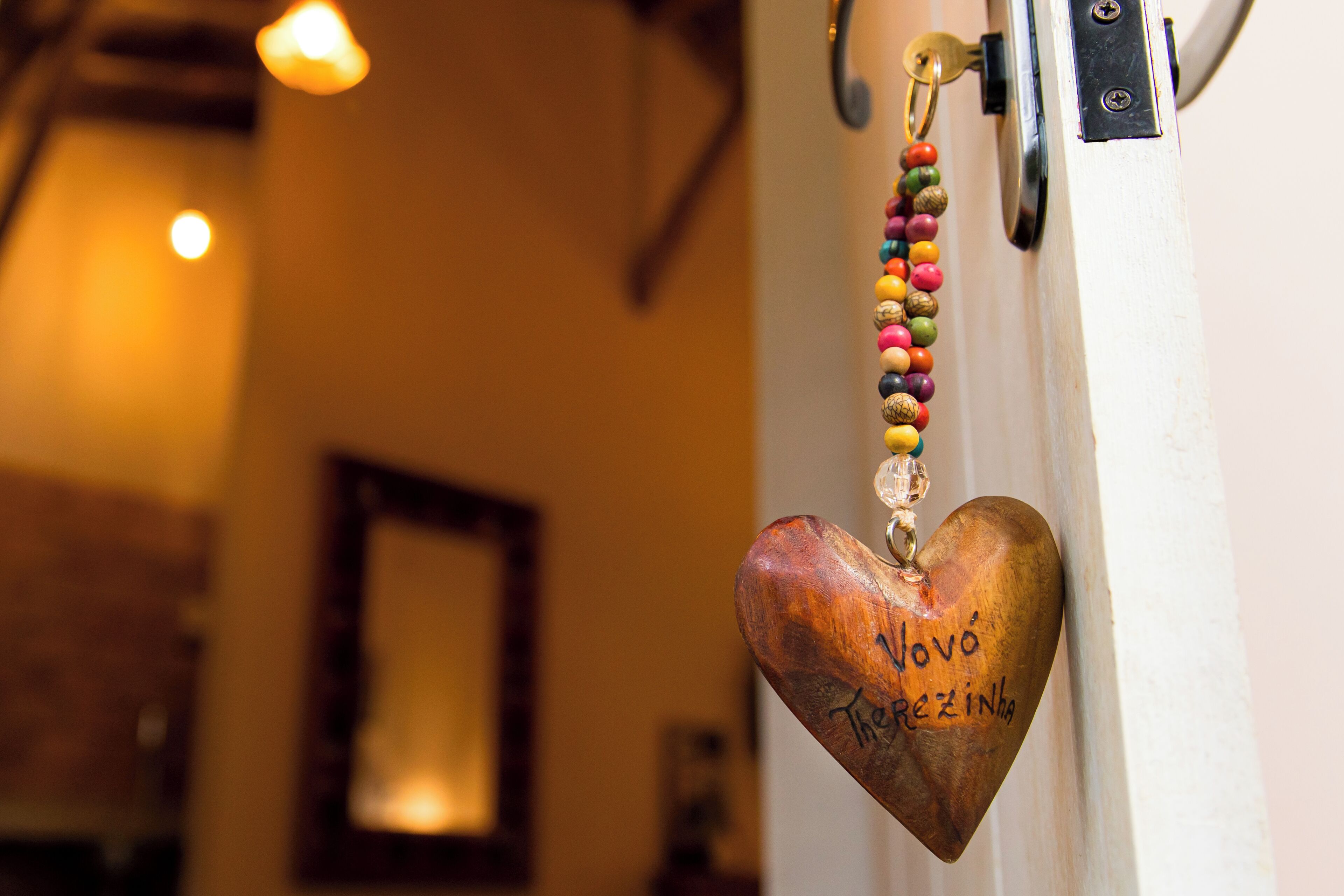 A wooden heart-shaped keychain with beads and the name "Novô Rezinho" hanging on a door.