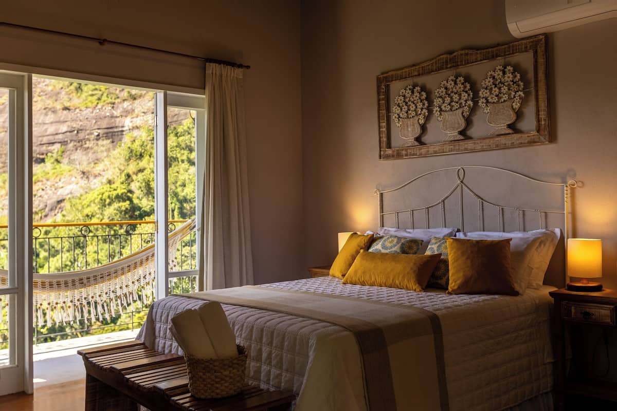 Een slaapkamer met een groot bed, een hangmat en uitzicht op een bergachtig landschap.