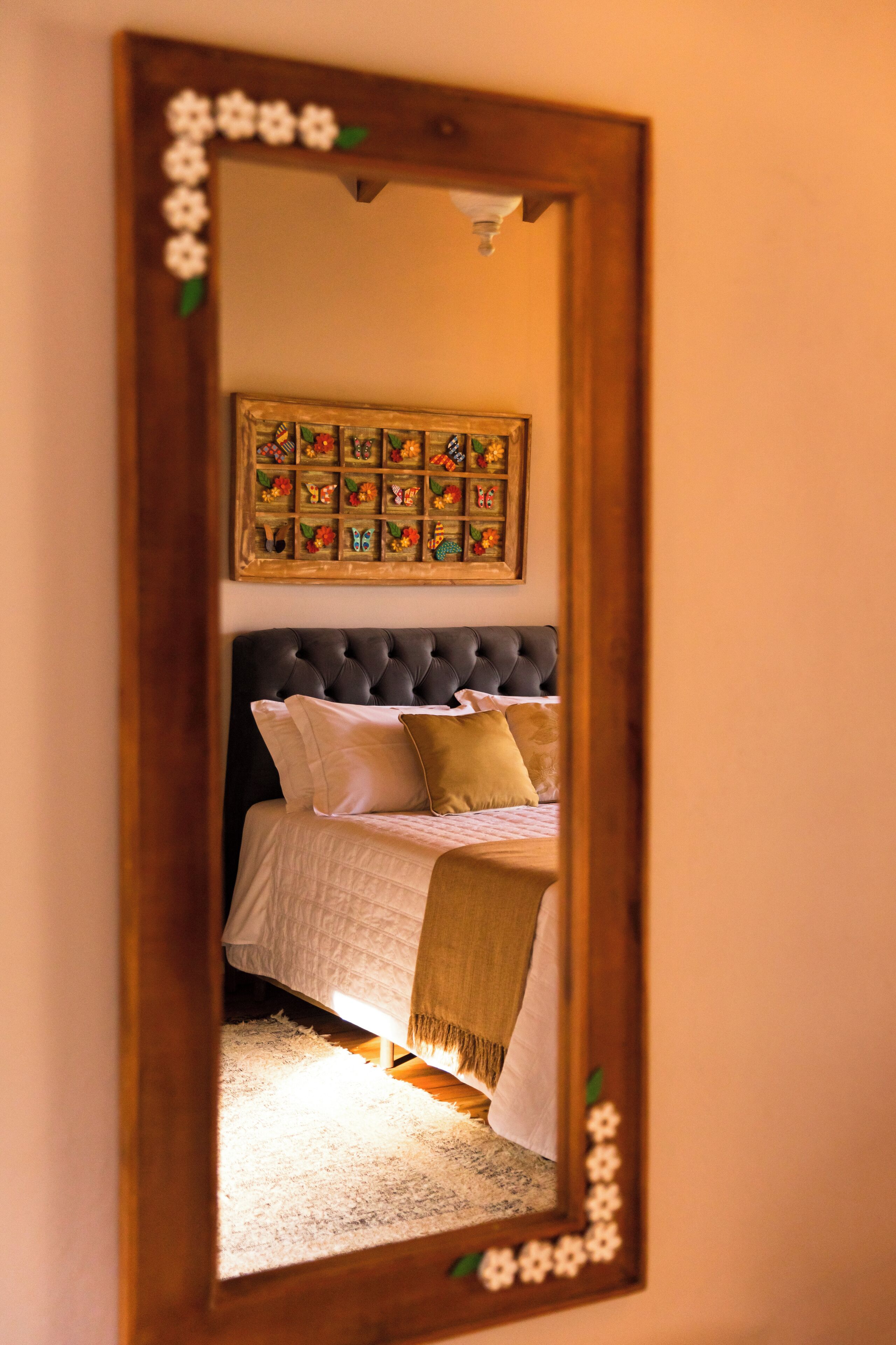A bedroom with a large mirror, a tufted headboard, and a floral artwork above the bed.