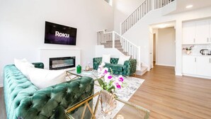 A modern living room with a green sofa, a TV, and a staircase leading to the upper floor. - Orchards Retreat | AirCon | Sleeps 10 | Near Airpt (Edmonton)