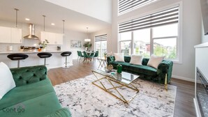 A spacious living area with a green sofa, a glass coffee table, and a dining area with a green table and chairs. - Orchards Retreat | AirCon | Sleeps 10 | Near Airpt (Edmonton)