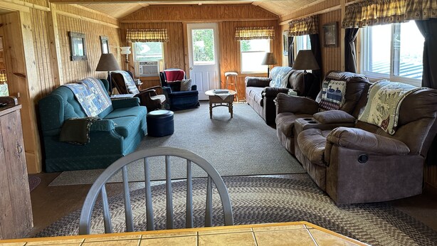 A cabin interior with a wooden ceiling, a 'Welcome Cabin' sign, two sofas, a dining table, and a window with curtains. - Marzullo's Mountaintop Cabin (Brookville)