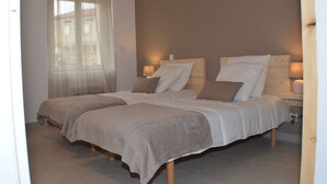 Une chambre avec deux lits, une fenêtre avec des rideaux légers et des lampes de chevet.