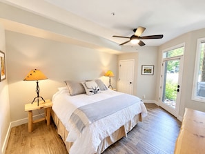 A bedroom with a bed, bedside lamps, a ceiling fan, a door, and a window. - Steps to Steamboat Slopes! Ski-In Ski-Out, Year-Round Heated Pool, Hot Tub & Gym (Steamboat Springs)