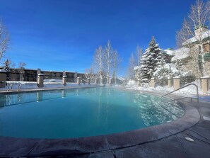 A clear blue pool surrounded by snow-covered trees and buildings. - Steps to Steamboat Slopes! Ski-In Ski-Out, Year-Round Heated Pool, Hot Tub & Gym (Steamboat Springs)