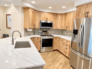 A modern kitchen with wooden cabinets, stainless steel appliances, a marble countertop, and a built-in microwave. - Steps to Steamboat Slopes! Ski-In Ski-Out, Year-Round Heated Pool, Hot Tub & Gym (Steamboat Springs)