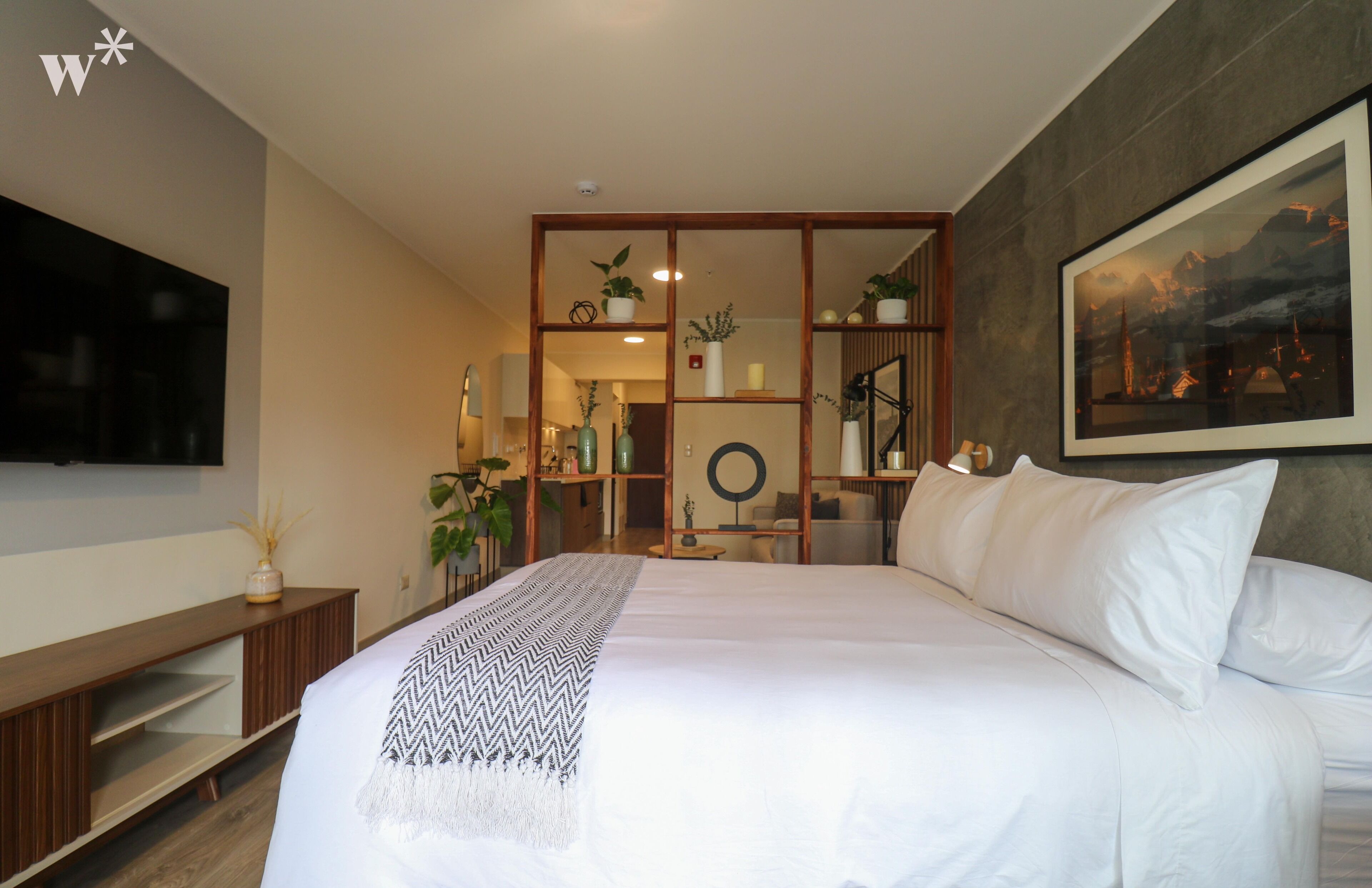Een moderne hotelkamer met een groot bed, een flatscreen televisie aan de muur, een houten console en een groot gepresenteerd schilderij.