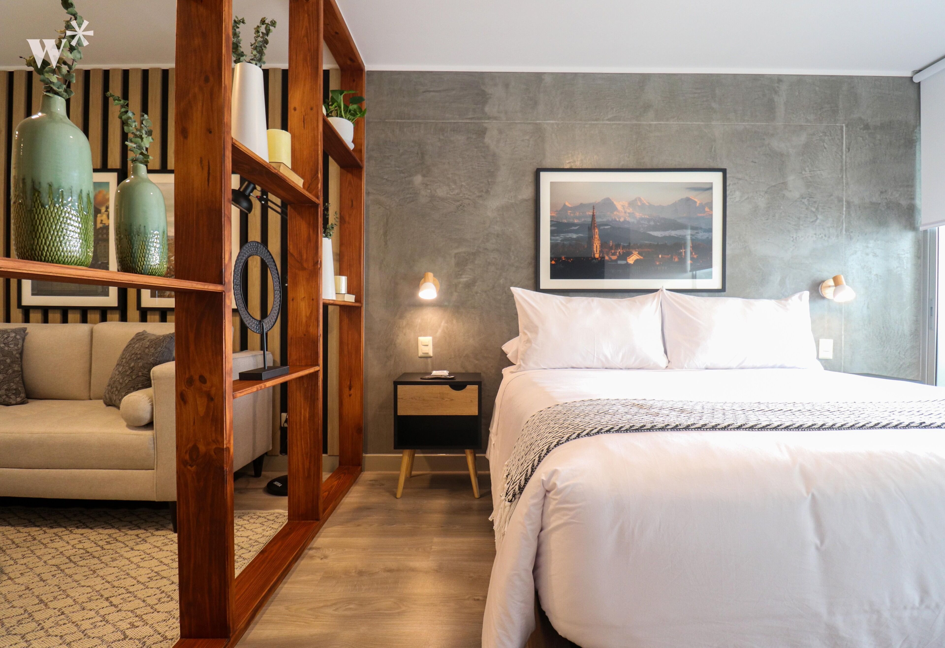 Une chambre à coucher comprenant un lit, une table de chevet, une étagère en bois ornée d’objets décoratifs, un canapé et un tableau accroché au mur.