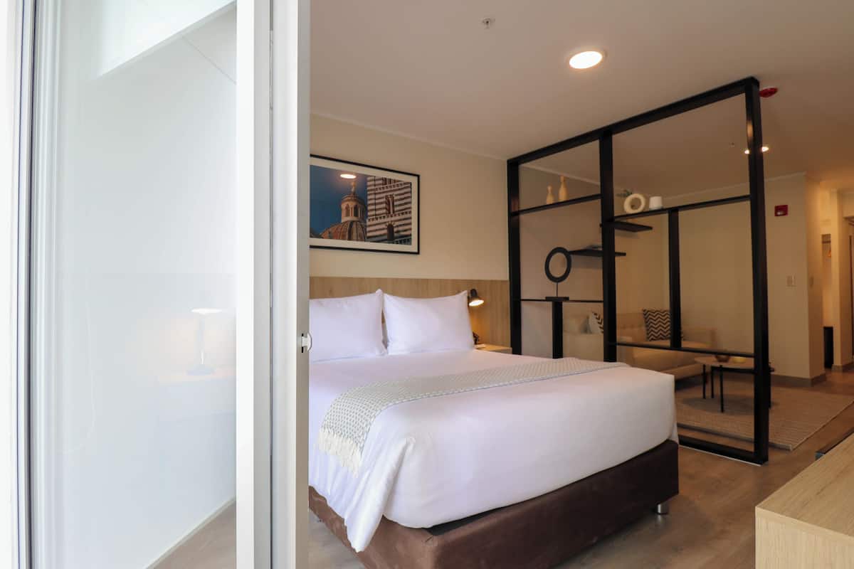 A modern hotel room with a large bed, a wooden headboard, a framed picture on the wall, and a mirror with a black frame.