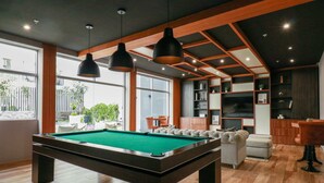 Un área de piscina interior moderna con mesa de billar, suelo de madera e iluminación colgante.