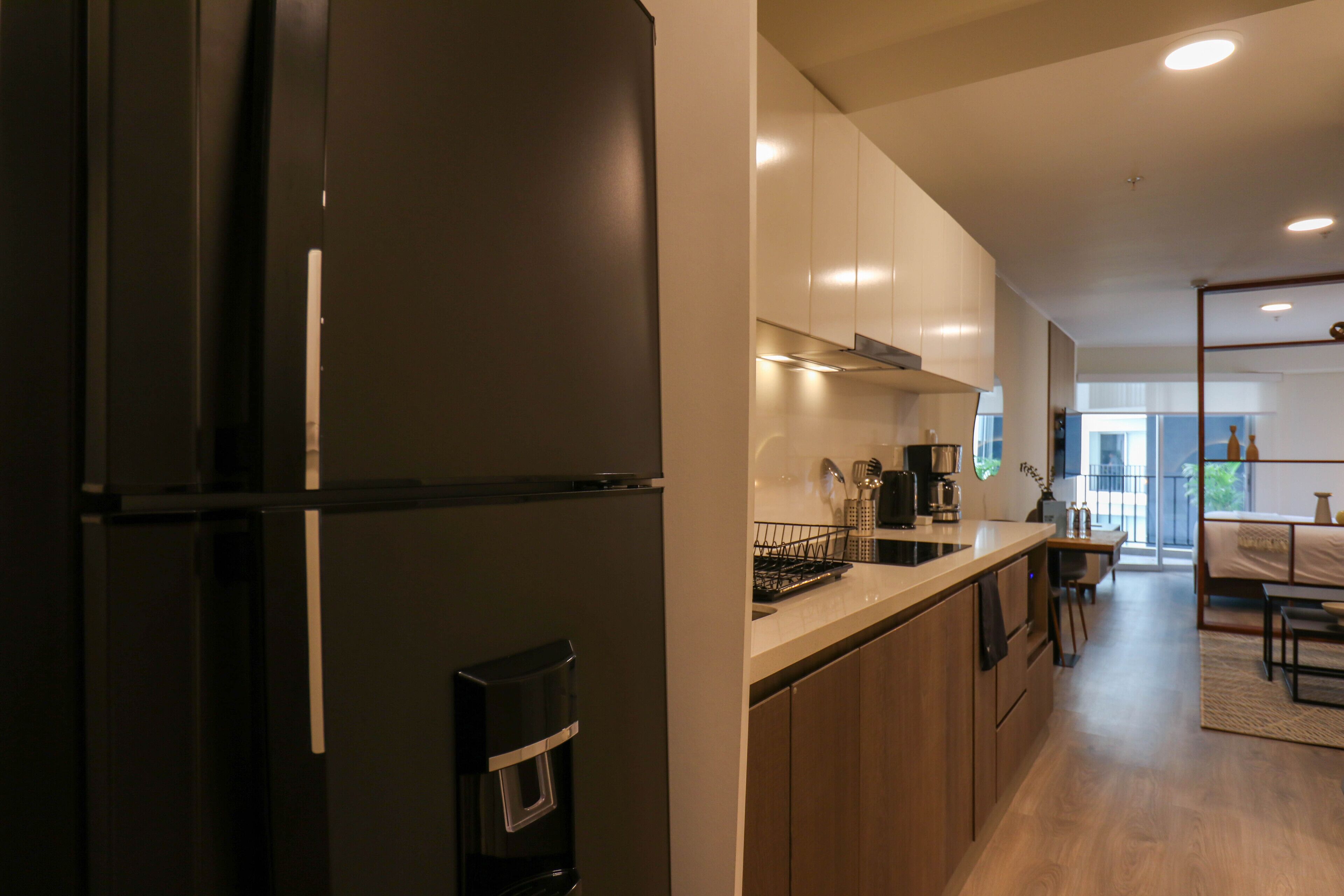 A modern kitchen with a black refrigerator, wooden cabinets, and a coffee maker.