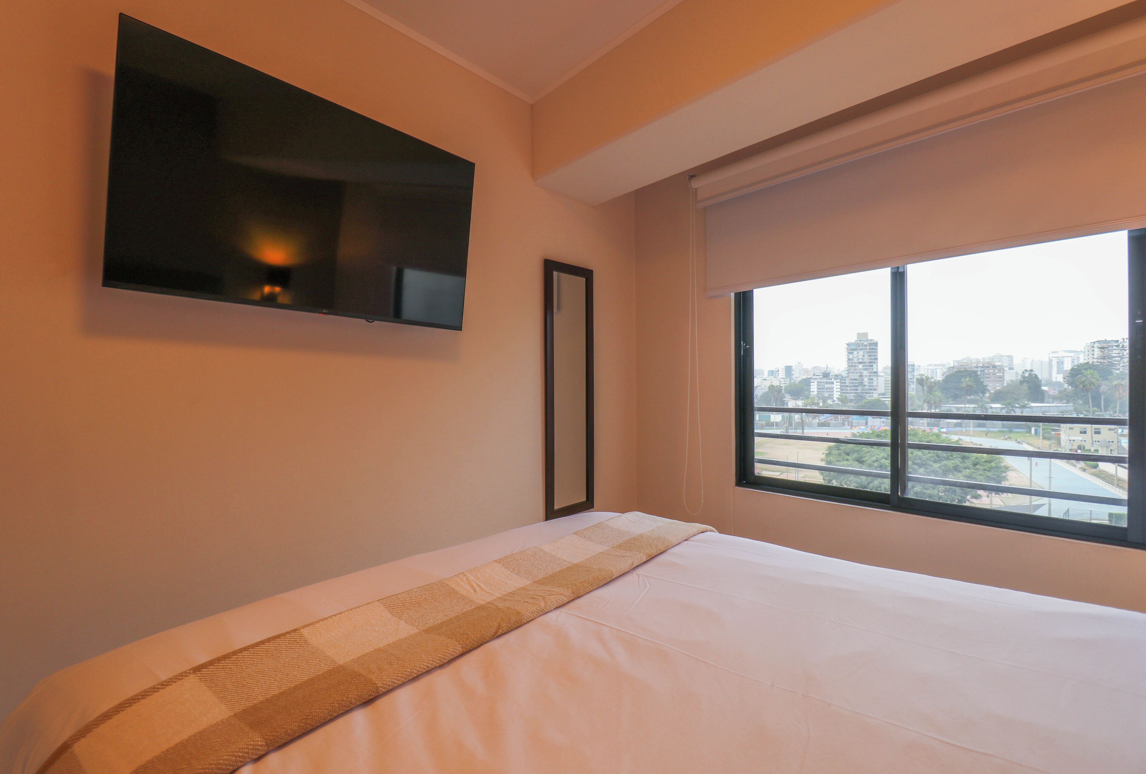 Hotelkamer met een bed, een flatscreen-tv aan de muur, een raam met uitzicht op de stad en een lijst met een foto.