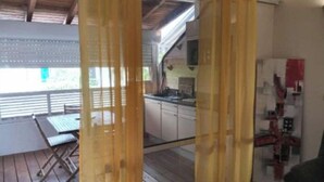 A room with a wooden floor, a dining table with chairs, a kitchen area with cabinets and a refrigerator, and a window with blinds. - 1 Bedroom Apartment in Saint-francois (Saint-francois)