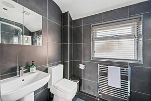 A modern bathroom with a white sink, toilet, and bidet, a mirror, and a window with blinds. - Stunning 5 Bed House in Leeds Contractors Welcome (Leeds)