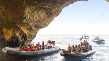 A cave opening with boats docked inside, passengers wearing life jackets, and a clear view of the sea.