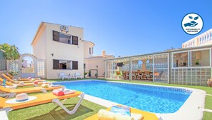 Une piscine avec des chaises longues, un espace extérieur aménagé et couvert, et un bâtiment doté d’un balcon.