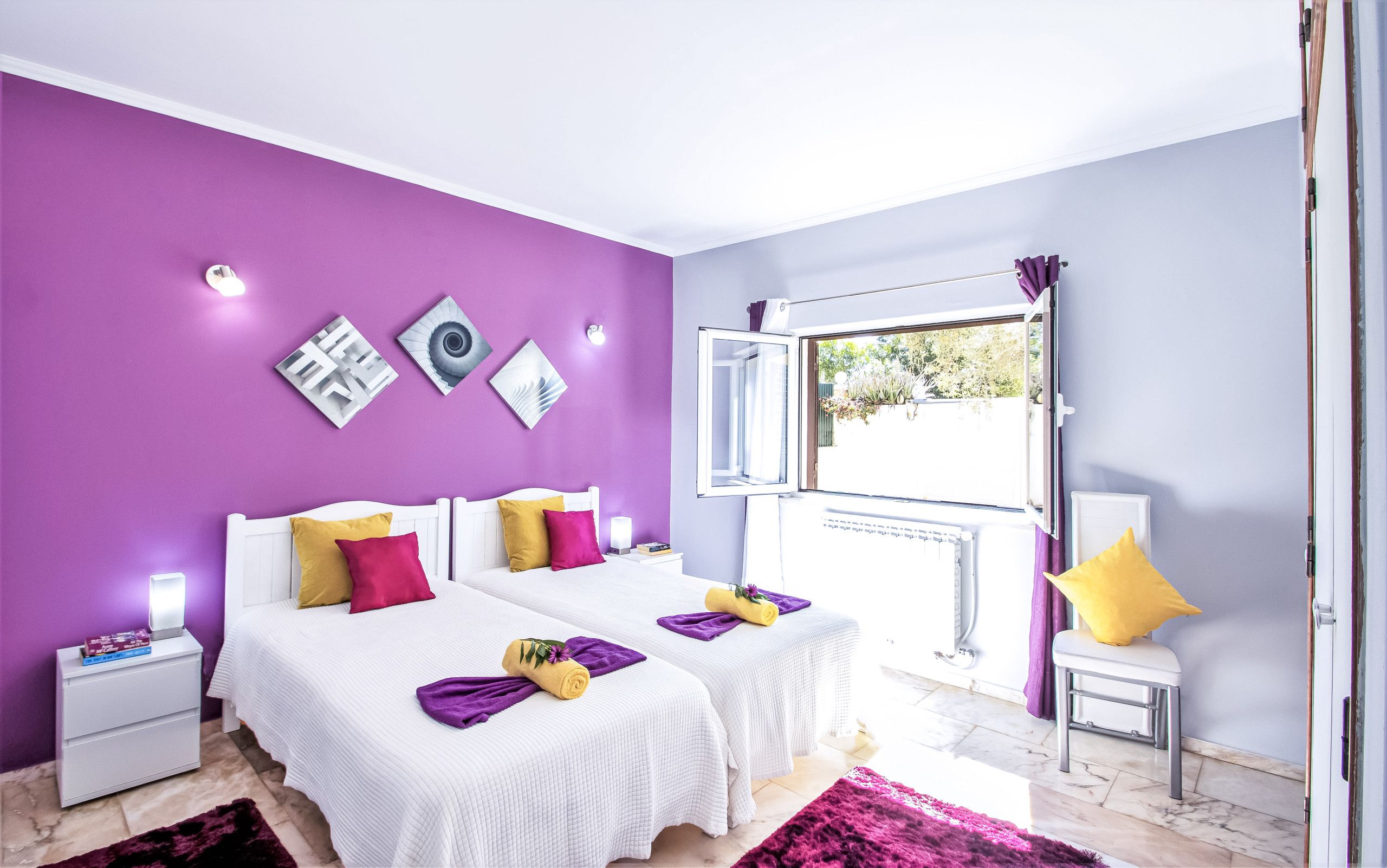 Une chambre avec deux lits, une fenêtre avec un rideau ouvert et des œuvres d’art accrochées au mur.