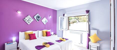 Quarto com duas camas, uma janela com cortina aberta e uma obra de arte na parede.
