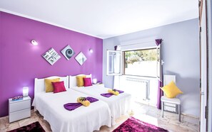 Een slaapkamer met twee bedden, een raam met open gordijn en kunst aan de muur.