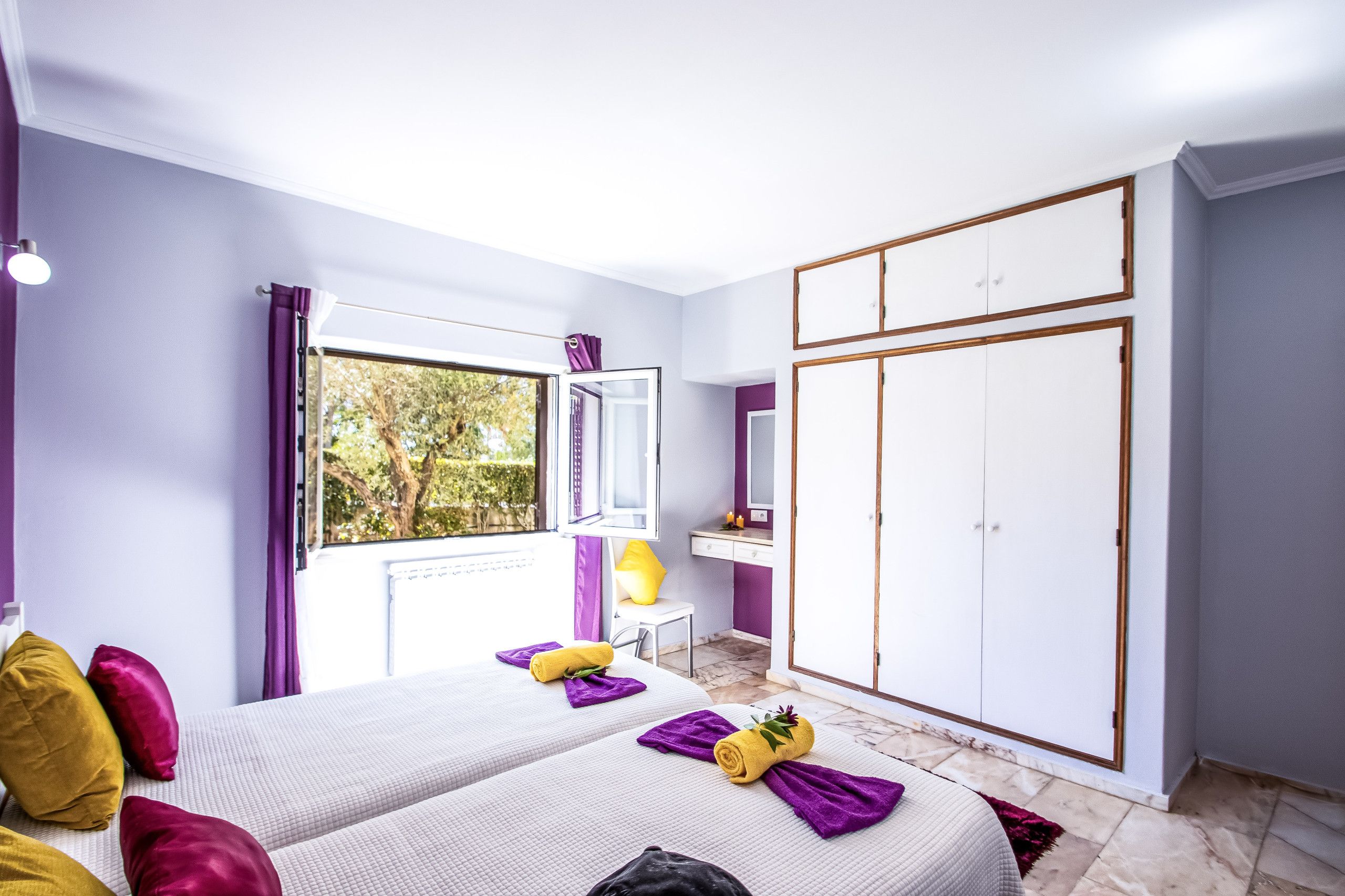 Een slaapkamer met een bed, een garderobe, een kaptafel met spiegel en een raam met uitzicht op bomen.