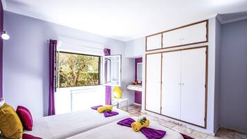 A bedroom with a bed, a wardrobe, a vanity with a mirror, and a window with a view of trees.