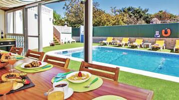 An outdoor dining area with a pool view, a table set with food and drinks, and a poolside lounge area with chairs and a no diving sign.
