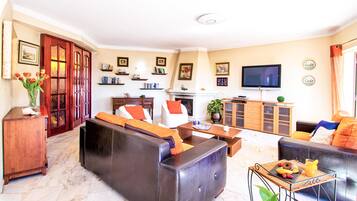 Uma sala de estar com lareira, sofá, televisão e diversos objetos decorativos.