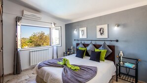 Een slaapkamer met een groot bed, uitzicht op bomen door het raam, een radiator en een nachtkastje met een lamp.