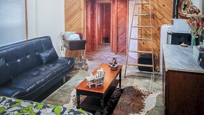 A cozy living room with a ceiling fan, a black leather sofa, a coffee table, and a wooden ladder.
