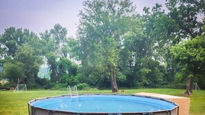 A circular hot tub with a wooden deck surrounding it, set in a grassy area with trees in the background.