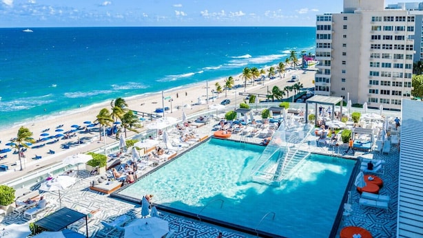 A rooftop pool with a view of the beach and ocean, surrounded by lounge chairs and umbrellas.