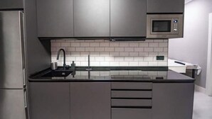 Ett modernt kök med grå skåp, ett kylskåp i rostfritt stål, en mikrovågsugn och en svart bänkskiva.