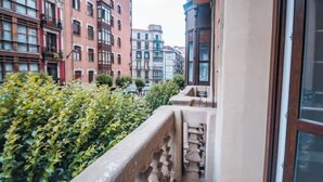 En smal stadsgata med höga byggnader, en stengallergång och tät, grön vegetation.