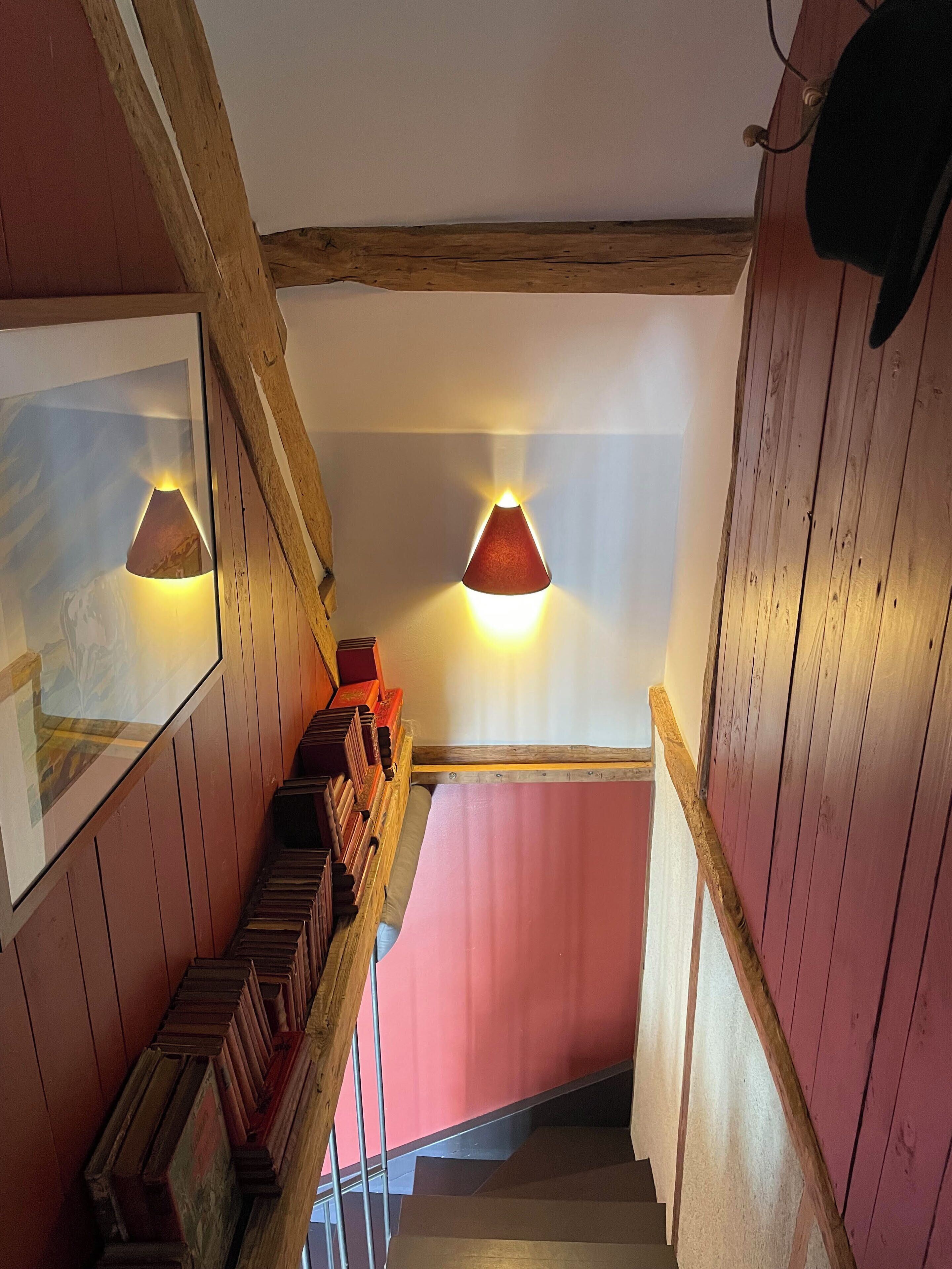 A wooden staircase with a pink wall at the top, wooden railings, and two wall-mounted lamps.