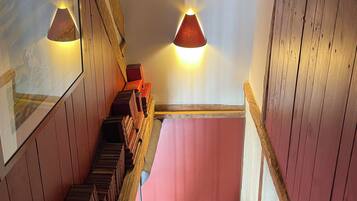A wooden staircase with a pink wall at the top, wooden railings, and two wall-mounted lamps.