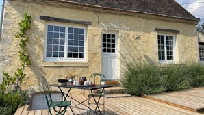Una casa con terraza de madera, una mesa con sillas y una ventana con puerta blanca.