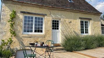 A house with a wooden deck, a table with chairs, and a window with a white door.