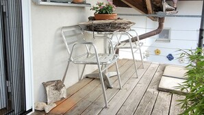 Une terrasse en bois avec des chaises et une table en métal, une fenêtre offrant une vue dégagée et un panneau solaire sur le toit.