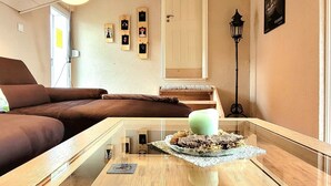 Un salon moderne avec un plancher en bois, un canapé marron, une table basse en verre avec une bougie et une lampe fixée au mur.