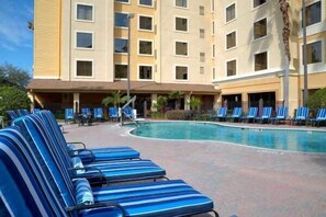Un hôtel doté d’une piscine, de chaises longues et d’un bâtiment à plusieurs étages avec de nombreuses fenêtres.