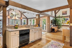 A spacious kitchen with wooden beams, a large island with a dishwasher, and a view of the outdoors. - Coast and Country Private Estate (Guilford)