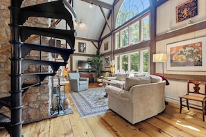 A spacious living area with a stone fireplace, wooden beams, and large windows offering natural light. - Coast and Country Private Estate (Guilford)