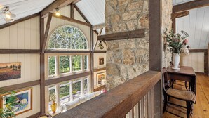 A room with a stone wall, wooden beams, a large arched window, and a wooden chair.