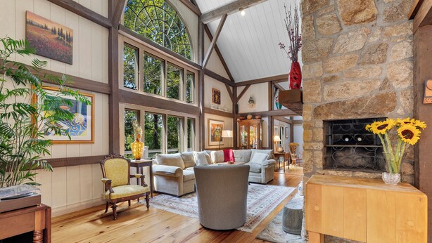 A spacious living room with wooden floors, large windows, and a stone fireplace.